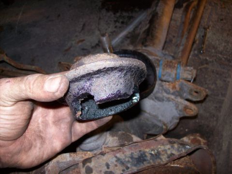 1986 Ford Bronco - A hand holds a heavily rusted and damaged suspension component, possibly a control arm bushing, with a visible tear in the rubber. The comp…