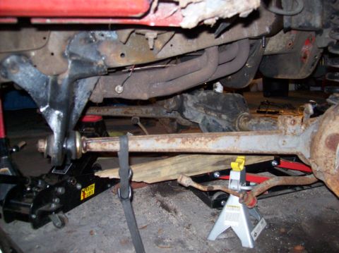 1986 Ford Bronco - The underside of a vehicle, likely a 1986 Ford Bronco, is shown with the suspension components supported by jack stands and a hydraulic jac…
