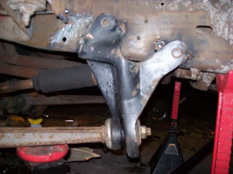 1986 Ford Bronco - A close-up view of the underside of a vehicle, showing a black metal bracket attached to the frame with visible welding marks. A black rubb…
