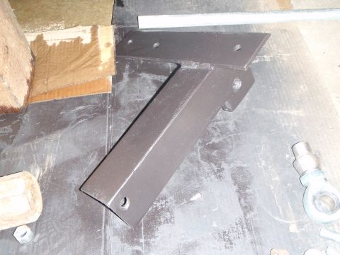 1996 Ford Bronco - A metal bracket painted dark brown is shown on a dark surface. There are also pieces of cardboard and wood visible in the scene.