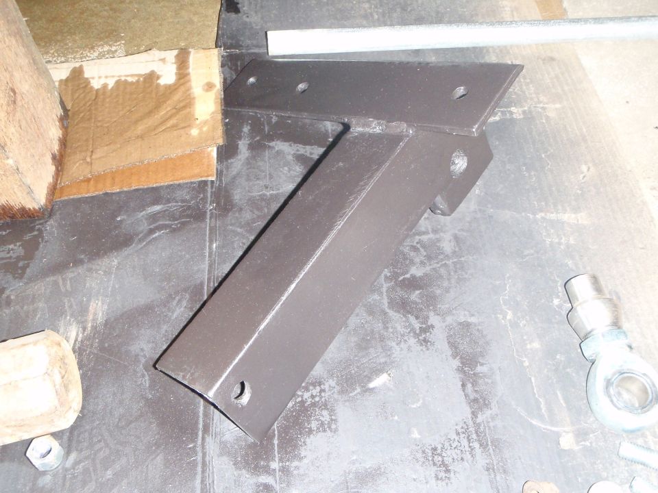 Dark brown painted metal bracket on a dark surface with cardboard and wood.