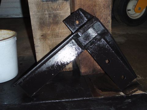 1996 Ford Bronco - A black metal bracket with two holes is resting on a wooden surface. A white bucket is visible to the left, and a tire is in the background.