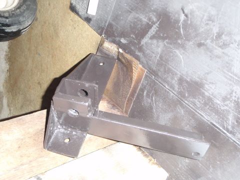 1996 Ford Bronco - A dark gray metal bracket with several holes is mounted to a wooden surface, with a portion of a tire and a concrete floor visible in the b…