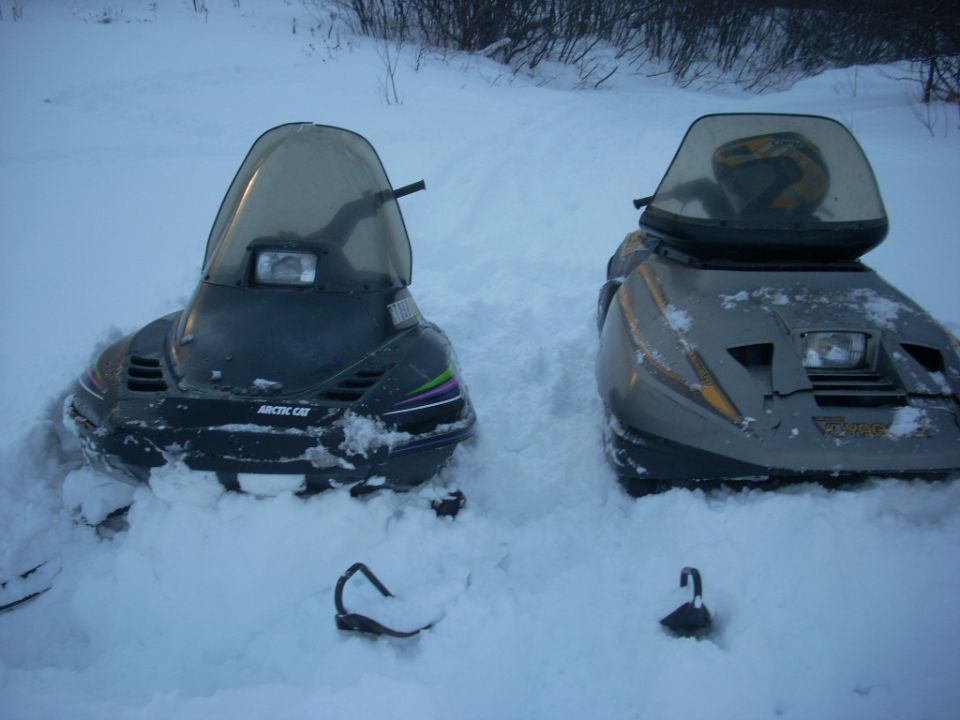 Black Arctic Cat snowmobile beside a gray Voyager sled in deep snow