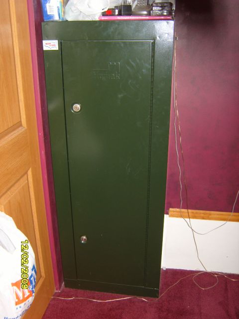 1989 Ford Bronco - A dark green metal safe is shown next to a wooden door and a burgundy wall. A white plastic bag with a date stamp is visible on the left.