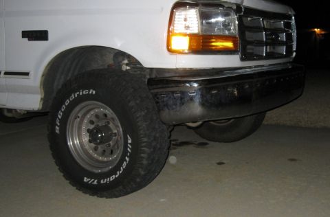 1996 Ford Bronco - The front passenger side quarter panel, tire, and chrome bumper of a white Ford Bronco are visible at night. The BFGoodrich All-Terrain T/A…