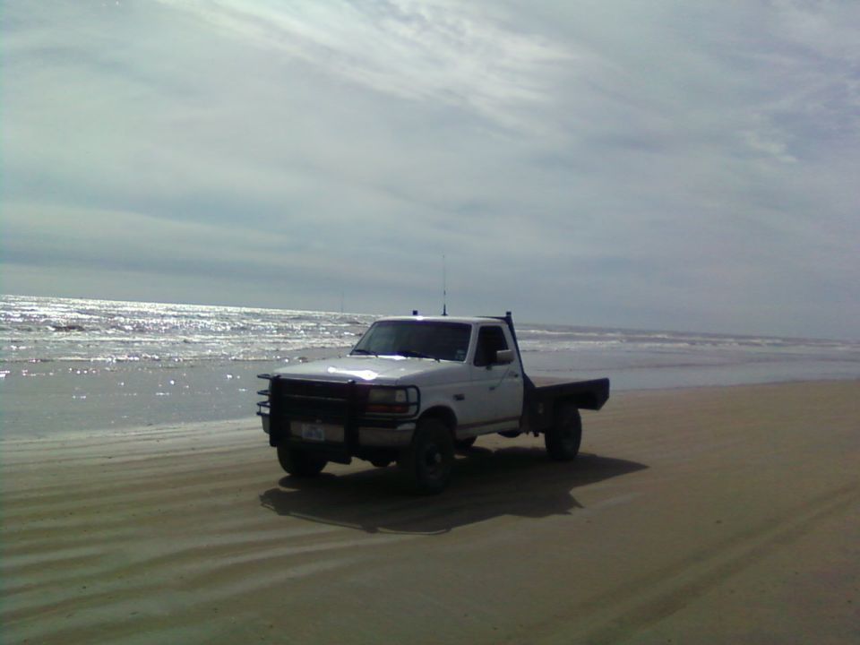 White flatbed pickup truck parked on a wide sandy beach