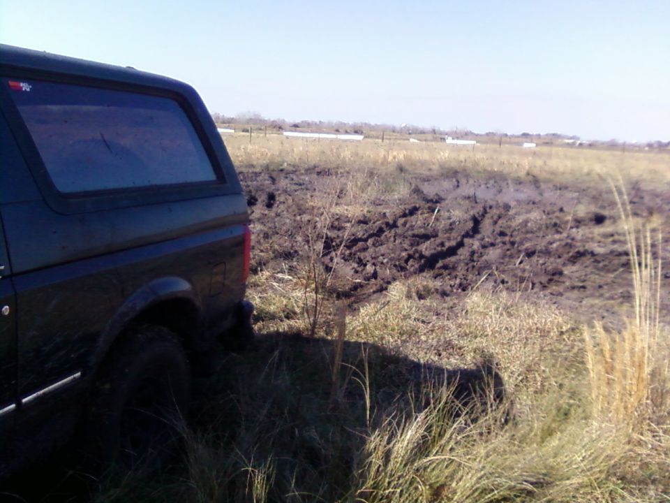Rear driver's side of a dark SUV in a muddy field.