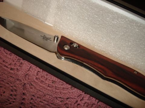 2000 Ford Crown Victoria - A close-up view of a folding knife with a wooden handle and a stainless steel blade, resting in a box.