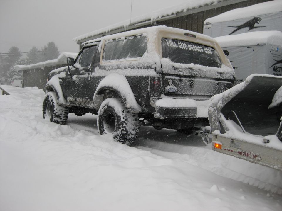 Snow-covered dark 1995 Ford Bronco parked outside in winter.