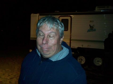 2004 Jeep Wrangler - Gray-haired man wearing a navy hooded sweatshirt standing at night in front of a white travel trailer.