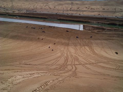 2004 Jeep Wrangler - An aerial view of a desert landscape with sand dunes, a canal, and a highway in the background. Several people are riding ATVs on the sand.