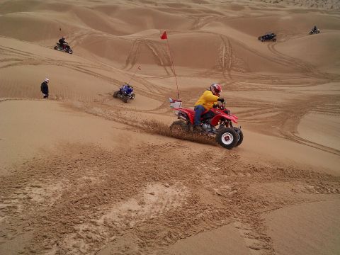 2004 Jeep Wrangler - A person in a yellow shirt and red helmet rides a red ATV down a sand dune, kicking up sand. Other ATVs and riders are visible in the backg…