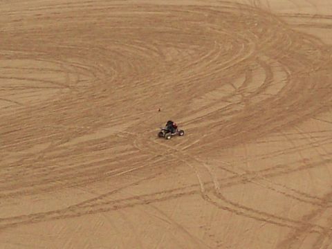 2004 Jeep Wrangler - An all-terrain vehicle with a rider is seen from above, kicking up dust on a sandy dune. The vehicle has a red flag attached to its rear.