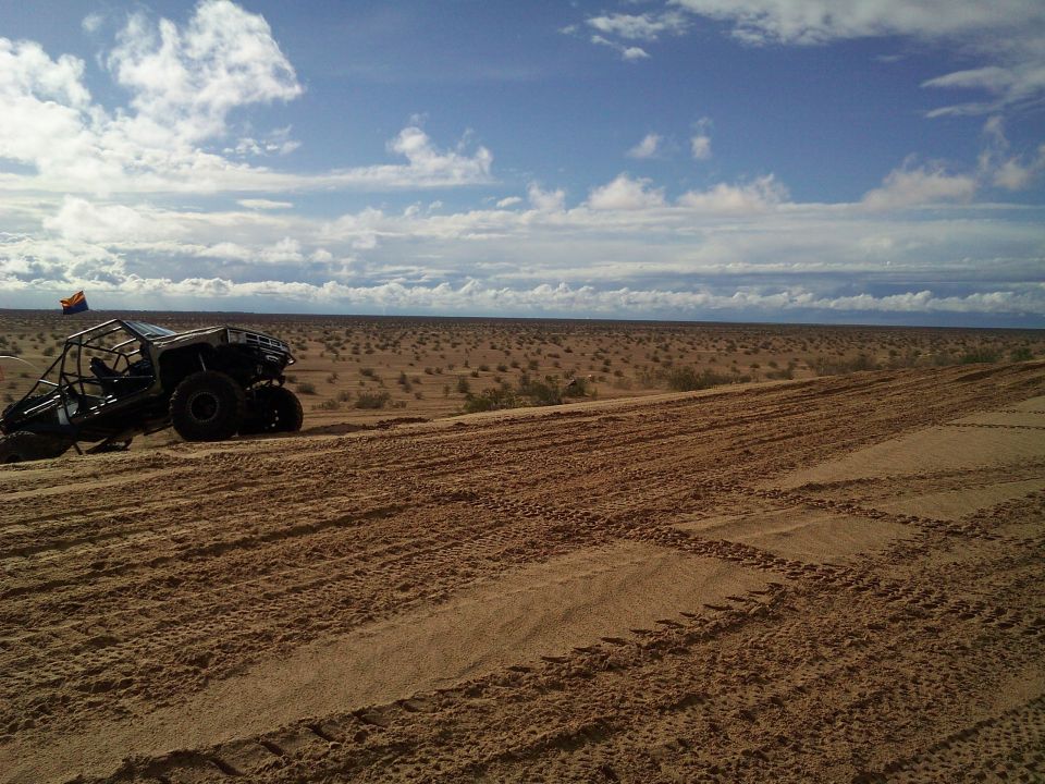 Off-road buggy on a sandy dune with tire tracks and a desert landscape.