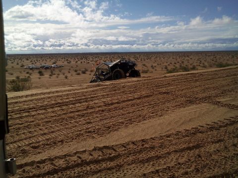 2004 Jeep Wrangler - A dune buggy is parked on a sandy dune in a desert landscape with scattered brush and a campsite in the distance under a cloudy sky.