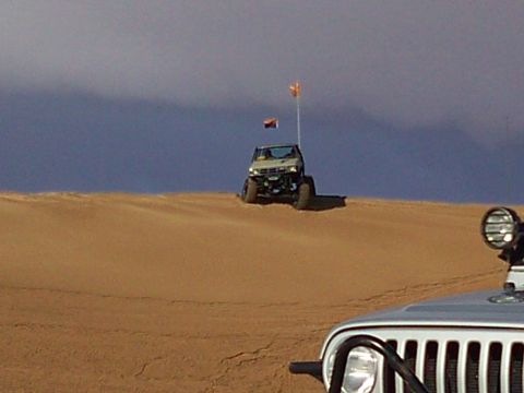2004 Jeep Wrangler - Two off-road vehicles are on a sand dune under a cloudy sky. The vehicle in the foreground is silver and partially visible, while the vehic…