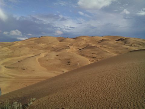 2004 Jeep Wrangler - A vast expanse of sand dunes under a cloudy blue sky.