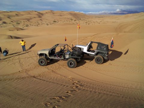 2004 Jeep Wrangler - Two custom off-road vehicles are parked on a sand dune with a person standing nearby. The vehicle in the foreground is a heavily modified b…