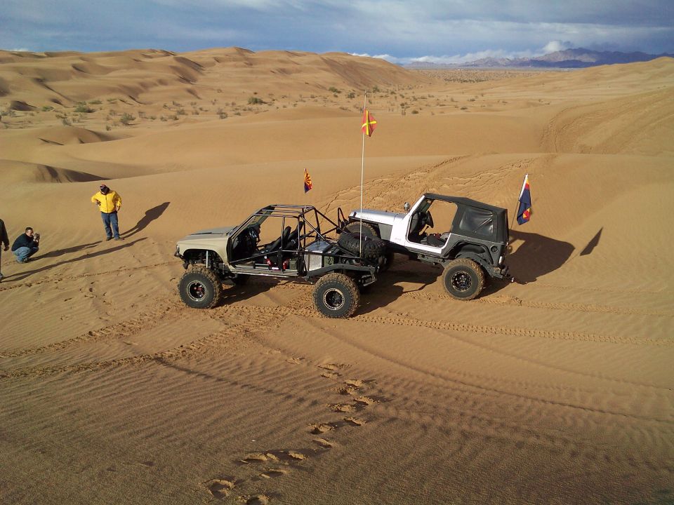 Two custom off-road vehicles on a sand dune with people.