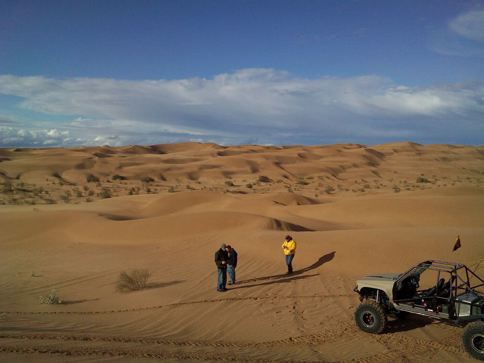 Custom off-road buggy with roll cage in a desert dune landscape.