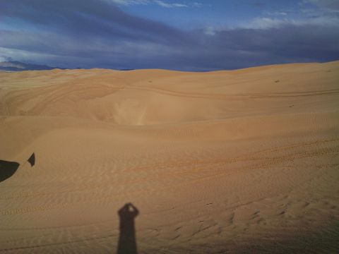 2004 Jeep Wrangler - A shadow of a person holding a camera is cast on sand dunes under a dramatic sky.