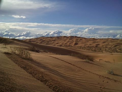 2004 Jeep Wrangler - A vast desert landscape with rolling sand dunes under a partly cloudy blue sky.