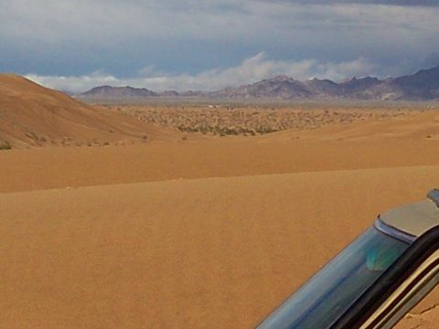 2004 Jeep Wrangler - A view from inside a vehicle looking out over sand dunes towards distant mountains under a cloudy sky. The vehicle's windshield and rooflin…