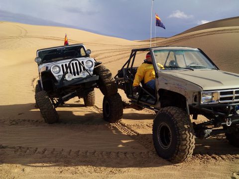 2004 Jeep Wrangler - Two off-road vehicles are positioned on sand dunes under a cloudy sky. A white Jeep Wrangler is in the foreground on the left, and a tan To…