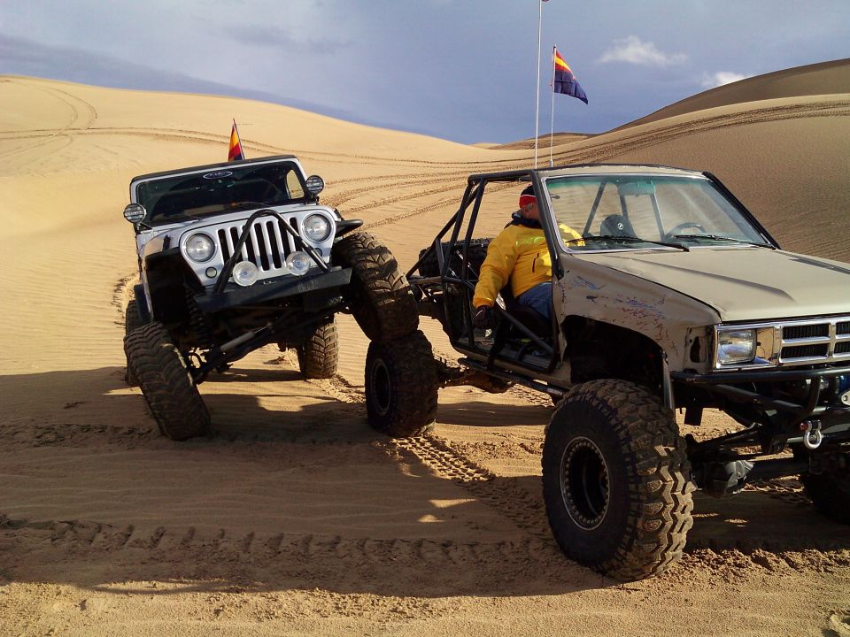 Two off-road vehicles, a white Jeep Wrangler and a tan Toyota pickup, on sand dunes.