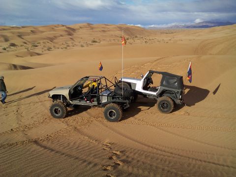 2004 Jeep Wrangler - Two custom off-road vehicles are parked on sand dunes under a partly cloudy sky. The vehicle on the right is a Jeep Wrangler with a black s…