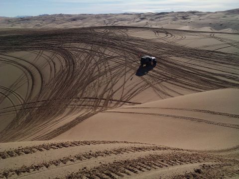 2004 Jeep Wrangler - A dark-colored Jeep Wrangler is parked on a vast sand dune landscape, surrounded by numerous tire tracks from off-roading. The vehicle is p…