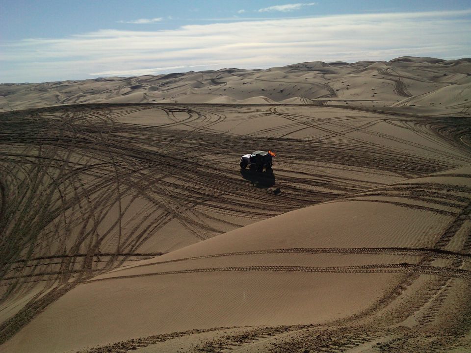 Off-road vehicle on a sand dune with many tire tracks.