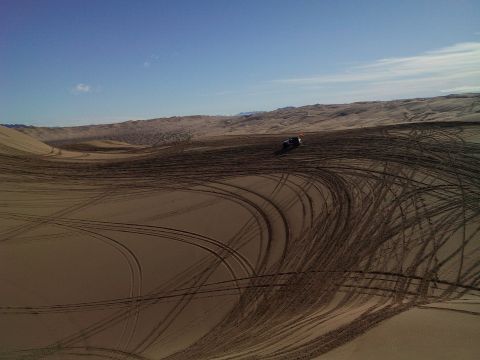 2004 Jeep Wrangler - An off-road vehicle with an orange flag is seen driving on sand dunes, leaving tire tracks in its wake. The vehicle is viewed from a high a…