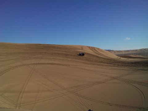 2004 Jeep Wrangler - A dark colored Jeep Wrangler is parked on a sand dune, leaving tire tracks on the sandy terrain under a clear blue sky.
