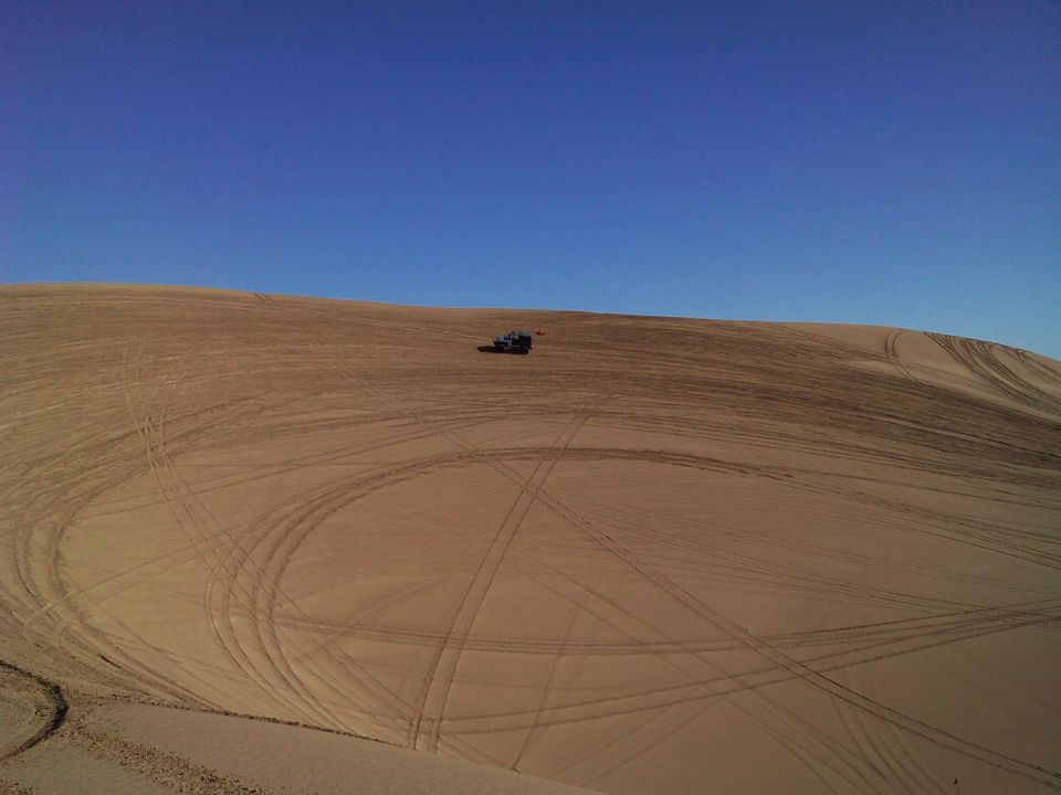 Jeep Wrangler parked on a sand dune with tire tracks.