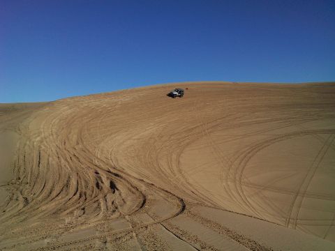 2004 Jeep Wrangler - A silver Jeep Wrangler is parked on a sand dune under a clear blue sky. Tire tracks are visible across the sandy terrain.