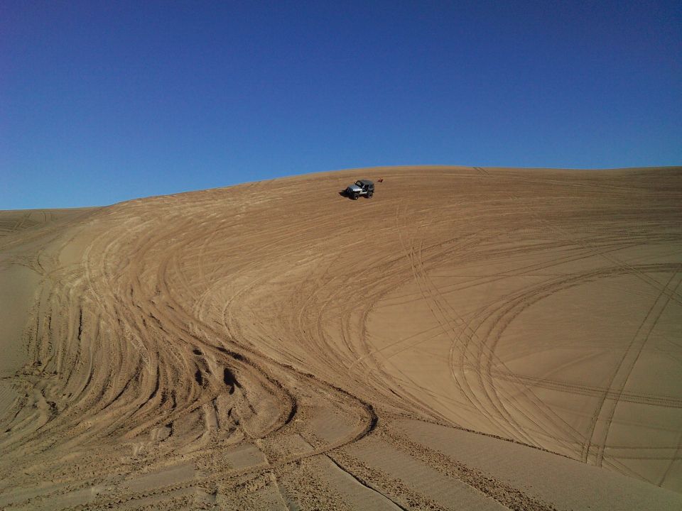 Silver Jeep Wrangler parked on a sand dune with tire tracks.