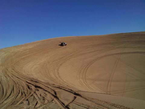 2004 Jeep Wrangler - A dark-colored Jeep Wrangler is parked on a sandy dune under a clear blue sky. Tire tracks are visible across the dune.