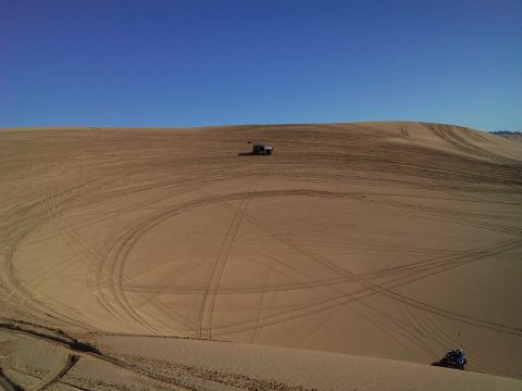 2004 Jeep Wrangler - A blue ATV is parked on a sand dune, with tire tracks visible across the sandy landscape. A dark colored Jeep Wrangler is parked on a dista…