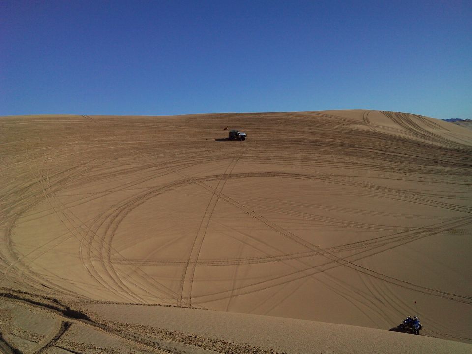 Blue ATV on sand dune with tire tracks and a Jeep Wrangler in the distance.