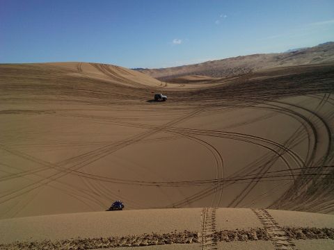 2004 Jeep Wrangler - A silver Jeep Wrangler is parked on a sand dune, with tire tracks crisscrossing the sandy landscape under a clear blue sky.