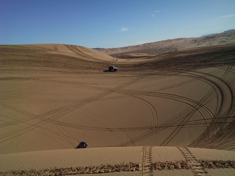 Silver Jeep Wrangler on a sand dune with tire tracks.