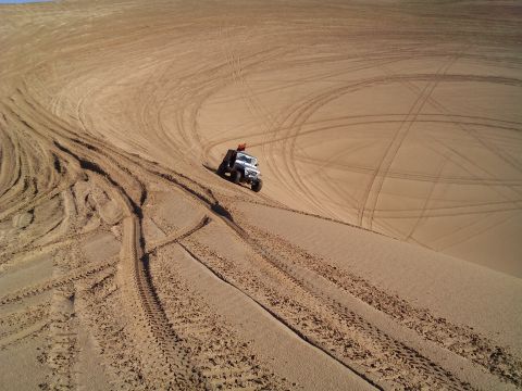 2004 Jeep Wrangler - A white Jeep Wrangler is driving down a sand dune, leaving tire tracks behind it. The dune is covered in many crisscrossing tire tracks fro…