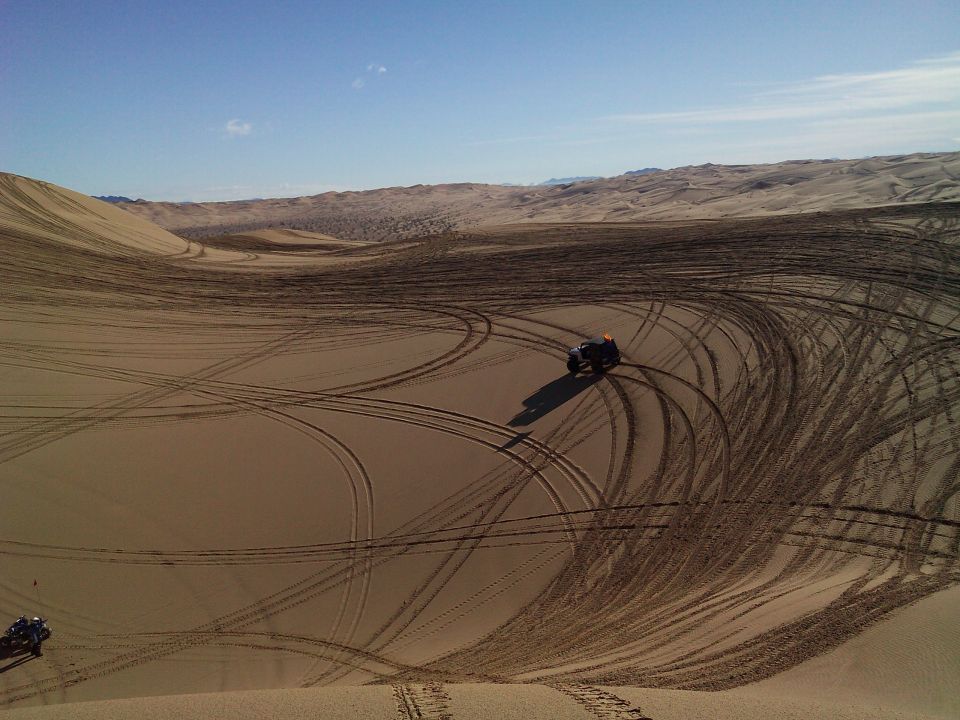 ATV driving on sand dunes, leaving tire tracks.