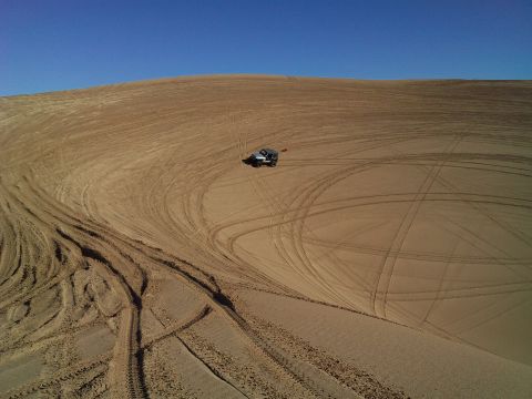 2004 Jeep Wrangler - An aerial view shows a dark-colored Jeep Wrangler parked on a vast sand dune, surrounded by numerous tire tracks. The vehicle is positioned…