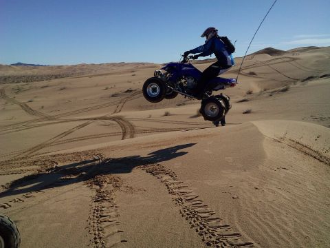 2004 Jeep Wrangler - A person on a blue ATV is mid-air, jumping over a sand dune. The ATV is angled upwards, with the rear wheels higher than the front.