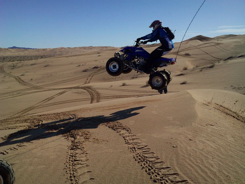 Person on a blue ATV jumping over a sand dune.