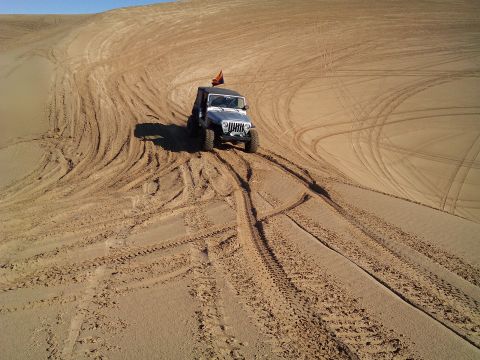 2004 Jeep Wrangler - A silver Jeep Wrangler with an Arizona flag is driving on a sand dune, leaving tire tracks.