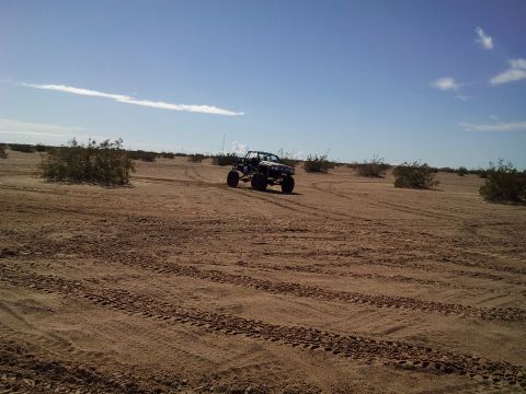 2004 Jeep Wrangler - A custom off-road buggy with large tires is driving across a sandy desert landscape with sparse vegetation under a clear blue sky.